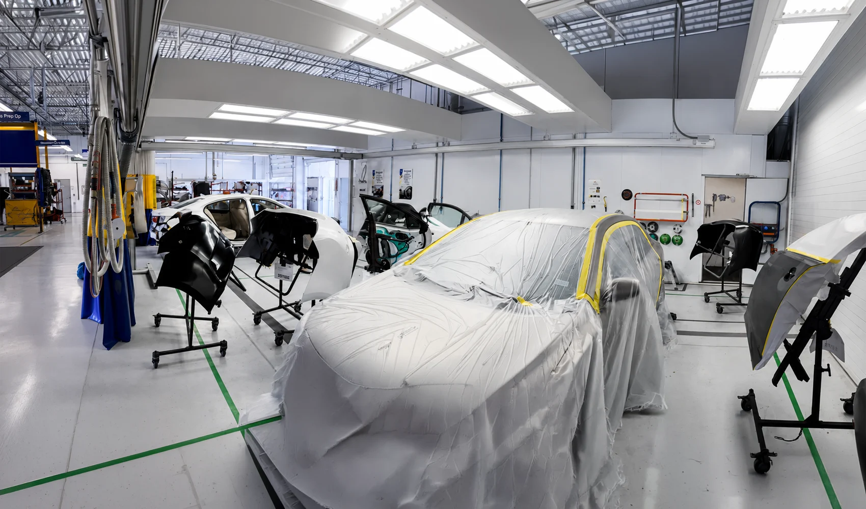 Masked vehicle surrounded by exterior panels in a clean paint preparation area.